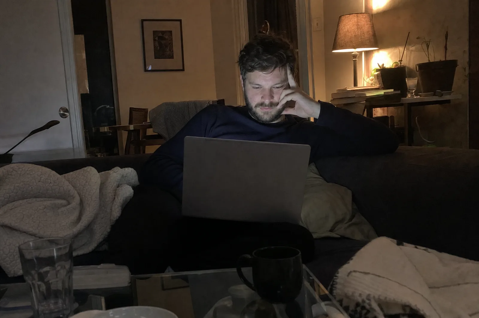 A freelancer slumped on his couch late at night, laptop on his knees, rewriting an email