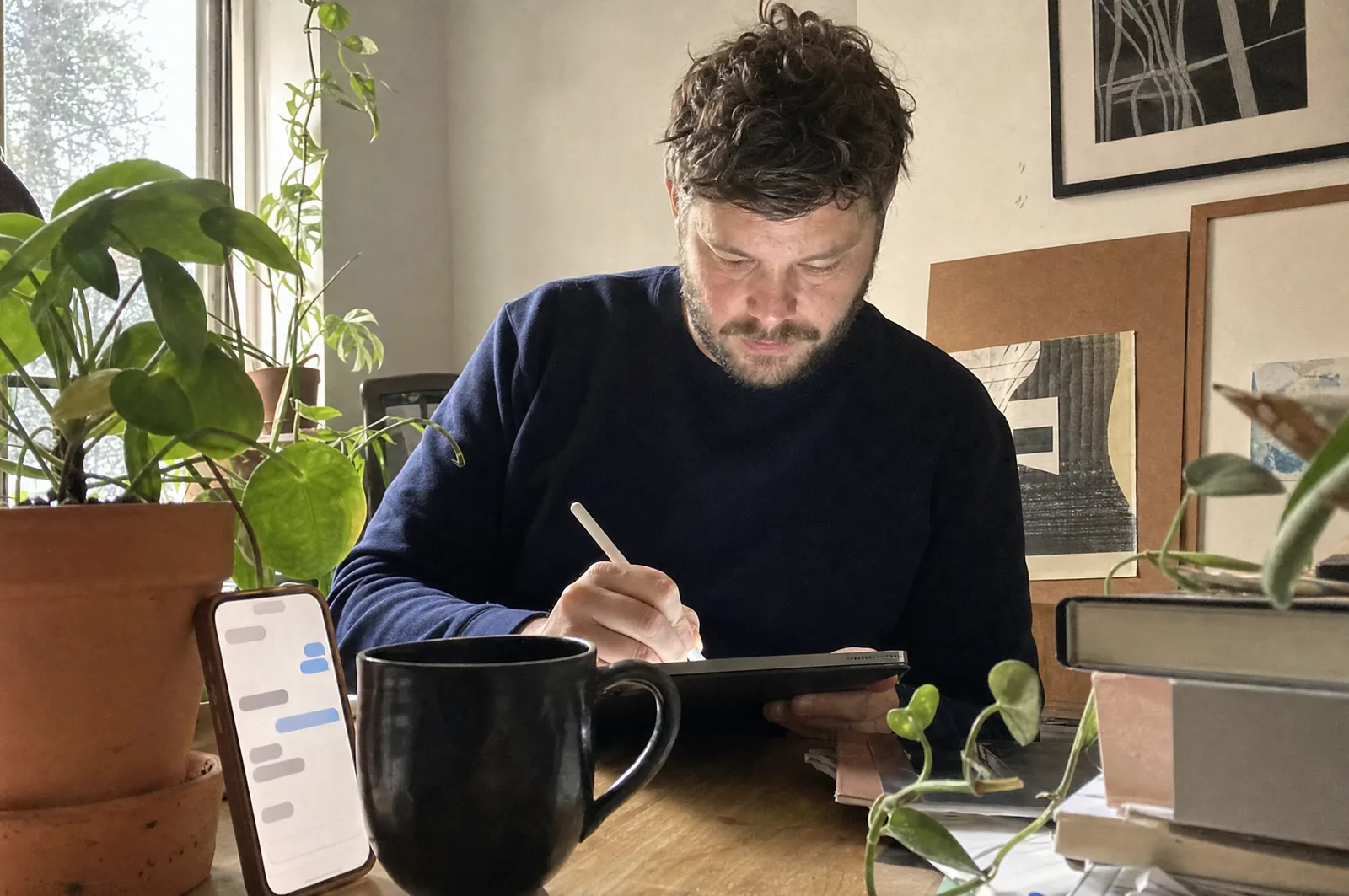 A freelance designer sketching in his home studio, phone propped beside him